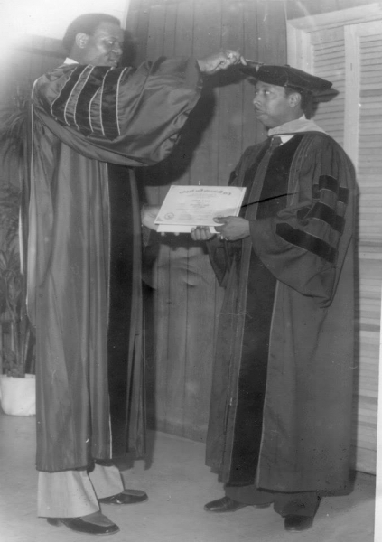Faculty member conferring a certificate on a candidate in doctoral regalia