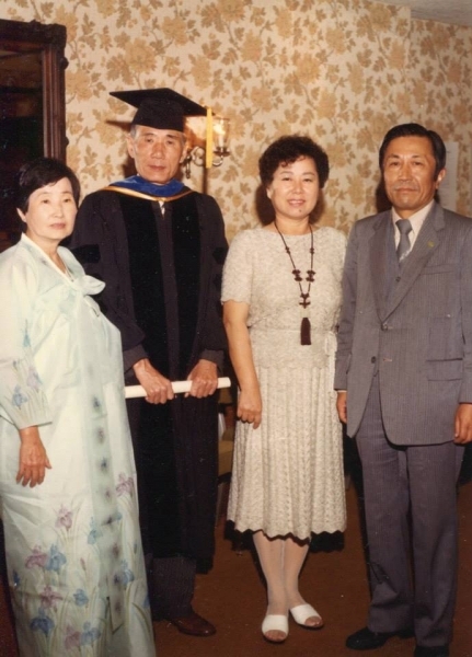 Graduate in cap and gown standing with three family members indoors