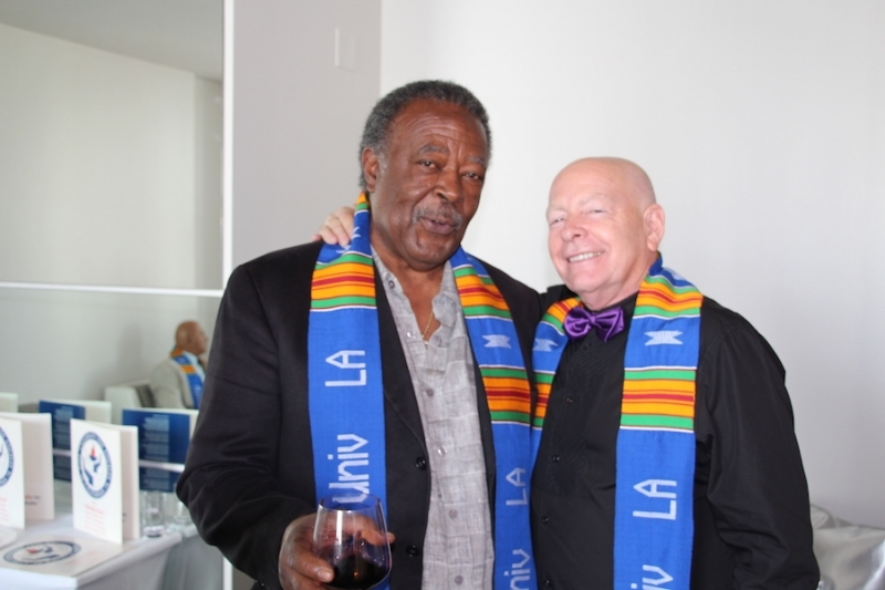 Two colleagues in university stoles with arms around each other at a reception