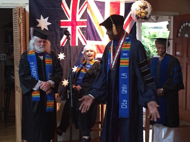 University officer in doctoral regalia giving remarks beside faculty colleagues