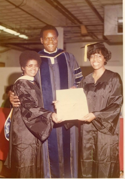 University officer presenting a diploma to two graduates in gowns
