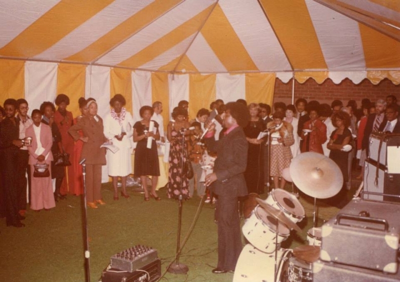 Guests singing together at a university reception under a striped tent