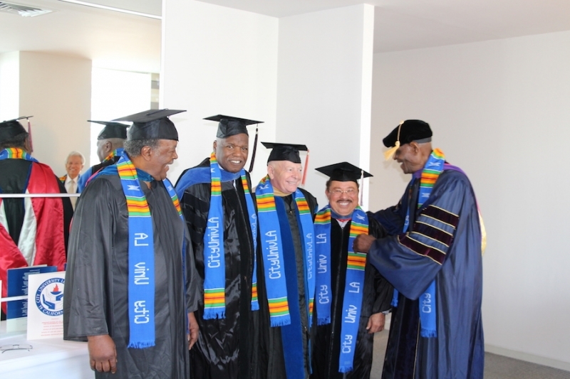 Faculty in regalia lining up as an officer adjusts a colleague's stole