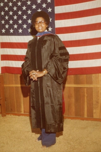 Woman in academic regalia standing before an American flag