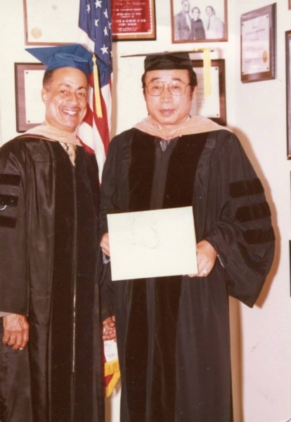 University officer standing with a doctoral honouree holding a certificate