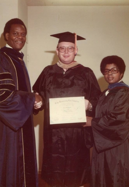 Graduate holding a City University Los Angeles certificate between two faculty members