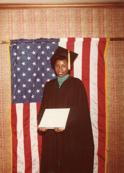 Graduate in cap and gown holding a diploma before an American flag