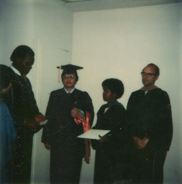 Graduates standing with faculty as diplomas are handed out