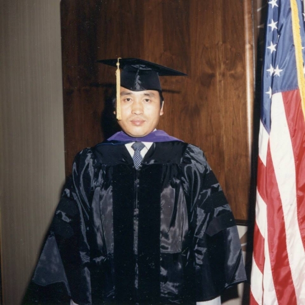 Graduate in regalia standing beside an American flag