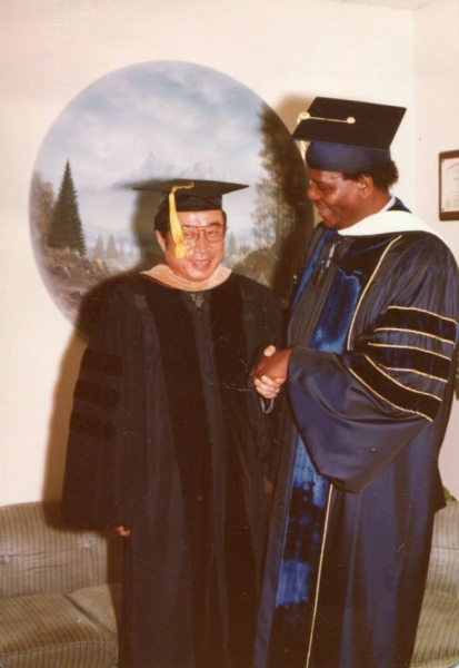 Two faculty members in doctoral regalia shaking hands