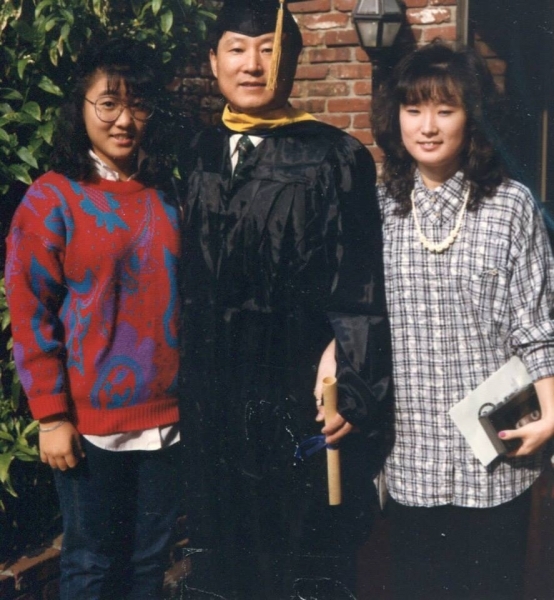 Graduate in regalia posing outdoors with two family members