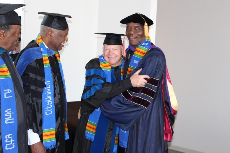Faculty members in regalia embracing and laughing before commencement
