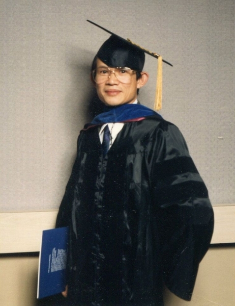 Doctoral graduate in navy regalia holding a commencement programme