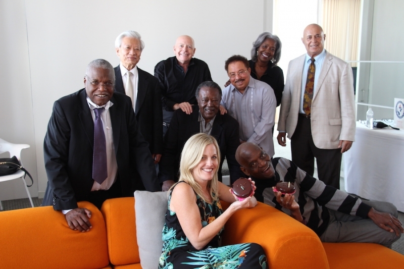 Nine members of the university community gathered around an orange sofa for a celebration photo