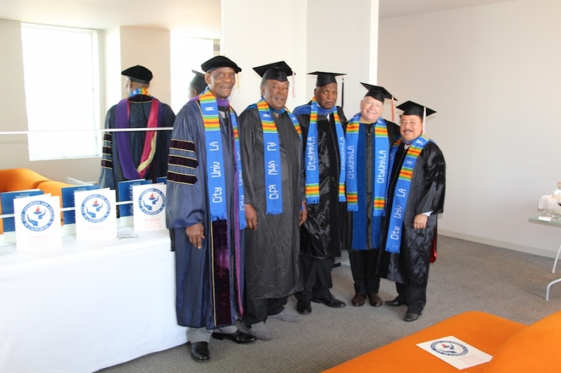 Five faculty members in regalia and university stoles standing beside a table of programmes