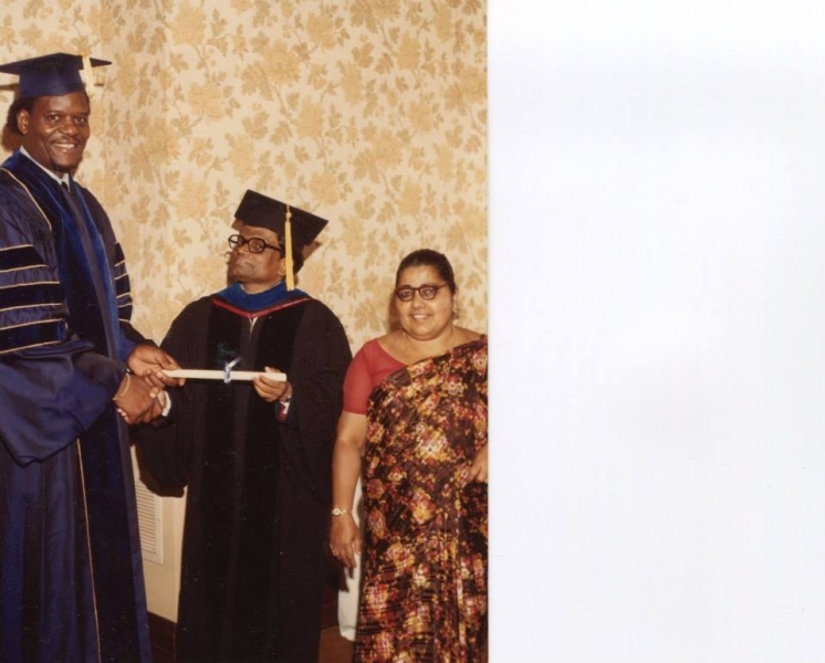 University president presenting a diploma scroll to a graduate accompanied by his wife