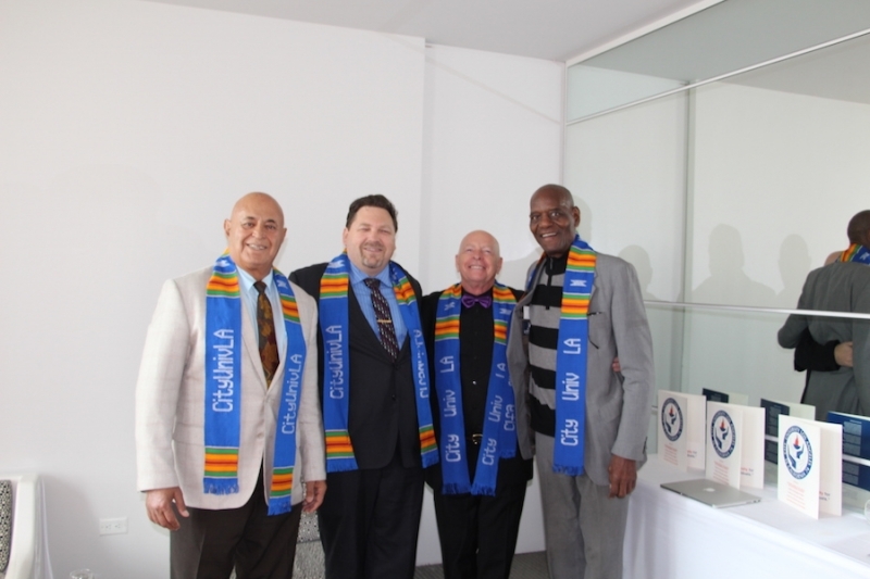 Four university leaders in kente stoles standing together beside a table of programmes