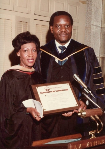 Two honourees in doctoral regalia holding a framed Certificate of Recognition