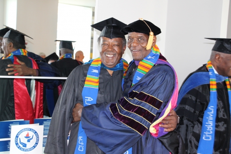 Two graduates in caps, gowns and university stoles embracing