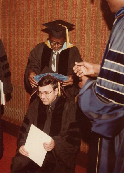 Faculty member placing a doctoral hood on a seated graduate
