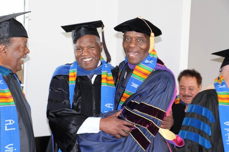 Two faculty members in regalia laughing together with colleagues