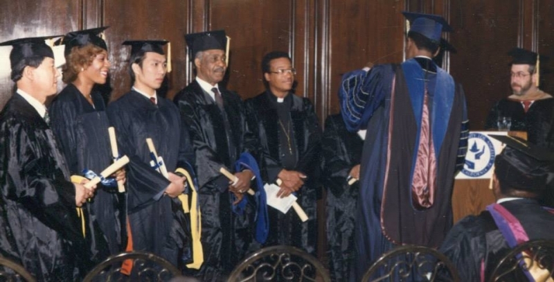 Graduates in regalia holding diplomas awaiting the hooding ceremony