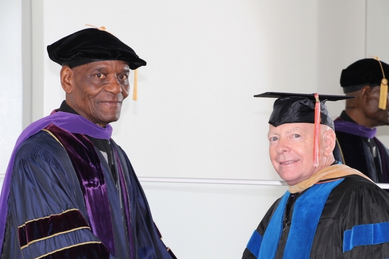 Two faculty members in doctoral tam and mortarboard regalia