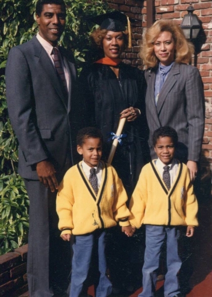 Graduate with her family and two young boys outside a brick building