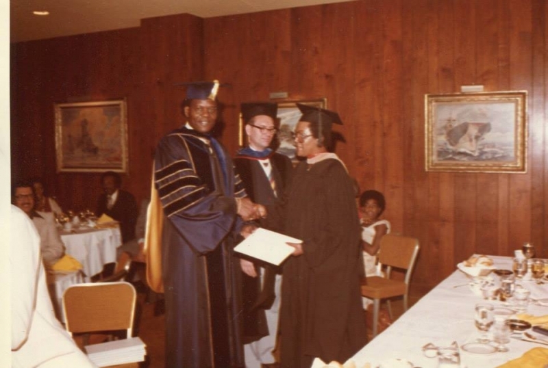 University president shaking hands with a graduate receiving a diploma at a luncheon