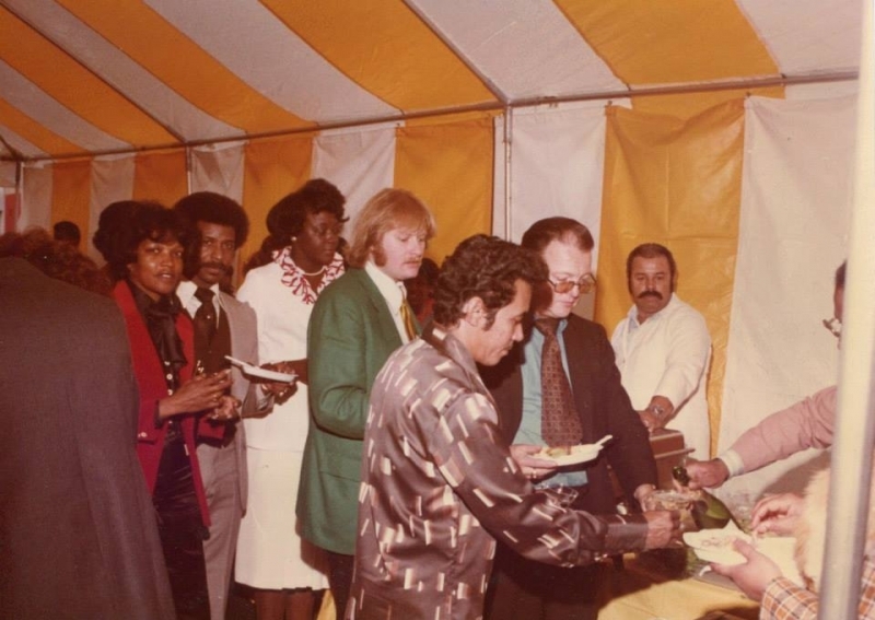 Guests being served at a buffet under a yellow and white striped tent