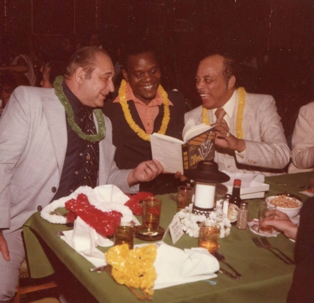 Three guests in leis reading a book together at a university banquet