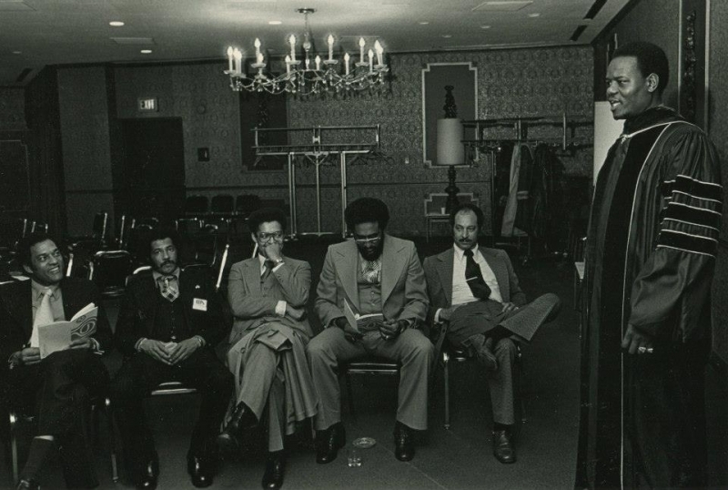 Faculty member in regalia addressing a small seated audience