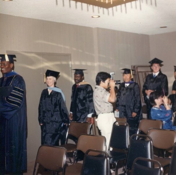 Graduates in regalia gathered in a ceremony room as a guest photographs them
