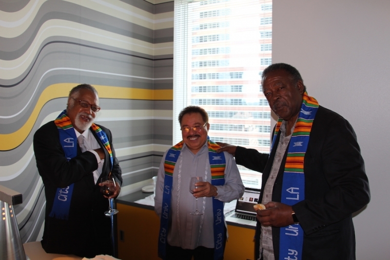 Three guests in university stoles talking beside a window overlooking downtown