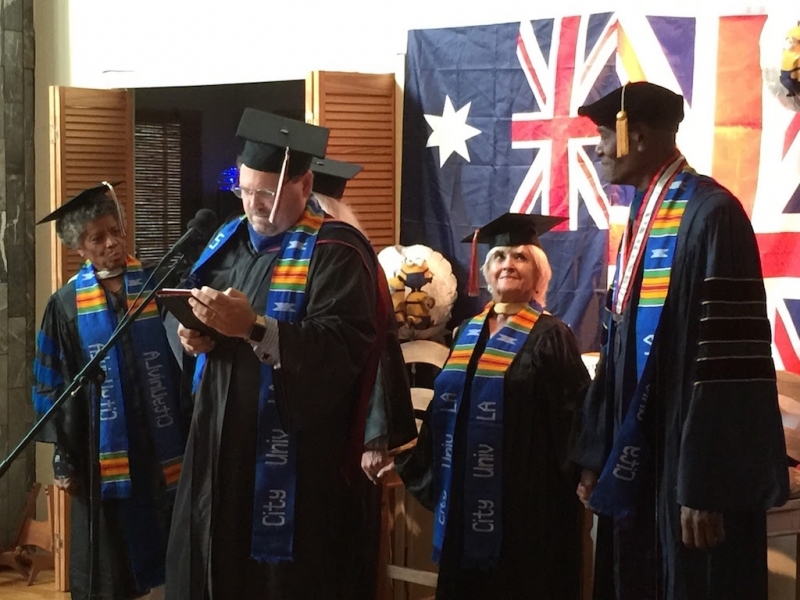Faculty member reading the conferral citation at a microphone in academic regalia
