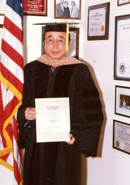 Honouree in doctoral regalia holding a City University Los Angeles certificate