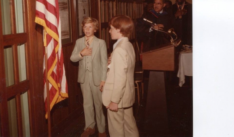 Two boys leading the pledge of allegiance beside an American flag
